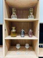 A beautifully crafted wooden shelf elegantly showcases an array of stunning vases accompanied by a delightful assortment of fine wine glasses that are arranged artfully across its surfaces photo
