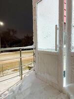 A beautifully snowy balcony featuring a sturdy railing and an inviting window, perfect for enjoying the winter scenery and the warm sunlight streaming through during the day photo