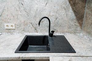 In a beautifully designed kitchen, there is a sleek, black sink accompanied by a stylish black faucet, both elegantly set on a counter that enhances the overall aesthetic of the space photo