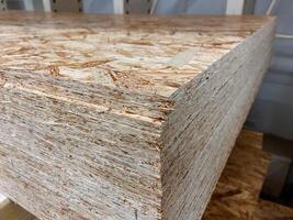 A neatly arranged stack of plywood sheets is resting on a sturdy wooden table that provides a stable surface for it. The scene is set on a solid floor, emphasizing the materials used photo