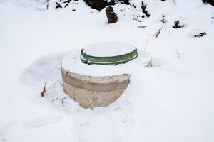 In a picturesque snowy landscape, a septic tank featuring a vibrant, bright green lid distinctly stands out against the pristine white snow, creating a unique and beautiful winter scene photo