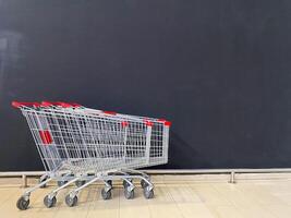 In a row, there are three shopping carts neatly lined up, positioned right in front of a large blackboard, creating an interesting visual and functional comparison between them photo