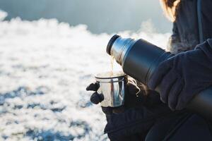 Hot tea poured from a thermos into a mug, cold winter, warm up with warm drinks, hiking in the mountains in winter, dishes for boiling water. photo