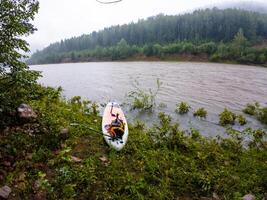 A vibrant and colorful kayak is peacefully resting on the sandy shore of a serene, calm lake. It is surrounded by beautiful nature, with lush greenery enhancing the inviting scene photo