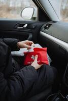A person is comfortably and securely seated inside a car, holding a wellequipped first aid kit, fully prepared and ready to provide help if needed in any emergency situation that arises photo