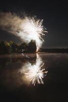 The vibrant and colorful fireworks light up the night sky while their brilliant reflections shimmer in the still water of a serene lake during a joyous celebration at midnight photo