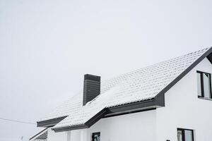 The roof of a beautiful white house is currently covered in a thick layer of snow that has fallen recently, creating a picturesque winter scene that showcases the charming architecture photo