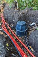 The process of installing underground utilities involves laying red cables alongside a black junction box within a carefully dug trench photo