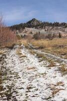 A Dirt Road Going Through A Snowy Field With A Mountain In The Background photo
