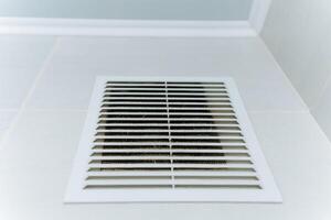 In a room, there is a white air vent installed on a white wall, creating a seamless look that blends with the surroundings, providing efficient air circulation throughout the space photo