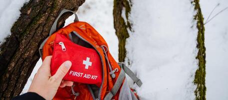 A person is standing and holding a first aid kit right in front of a wellused backpack which is likely packed with essentials for their outdoor activities or adventures ahead photo
