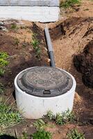 Manhole cover next to pipe in dirt, surrounded by grass and soil photo