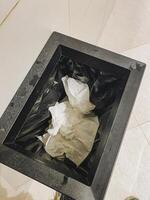 An overflowing black trash can filled with used tissues sits awkwardly on the tiled floor, creating a messy look that contrasts sharply with the otherwise clean surroundings photo