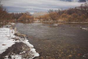 Winter scenery featuring a river, snowcovered trees, and a cloudy sky photo
