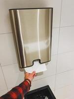 A person is currently utilizing a paper towel dispenser located in a bathroom, efficiently drying their hands after washing them, making use of this practical hygiene feature photo