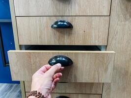 A person is opening a wooden drawer that features a sleek black handle, showcasing its craftsmanship and design, creating a sense of functionality and elegance in a home environment photo