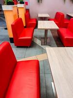 In the dining area of a restaurant, there is a neatly arranged row of vibrant red benches and tables, providing a comfortable setting for guests to enjoy their meals together photo