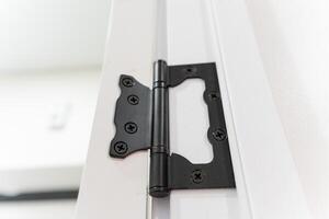 This image features a detailed closeup of a black door hinge that is affixed to a crisp white door, highlighting the contrast between the two distinct colors and materials involved photo