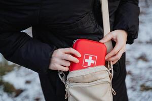 An individual is carefully placing a first aid kit inside their purse. This action demonstrates preparedness for any potential emergencies that may arise during their day photo