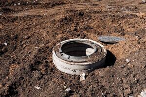 Concrete manhole cover on construction site surrounded by exposed soil and earth. Part of urban infrastructure development project. Essential for maintenance of underground utility network photo