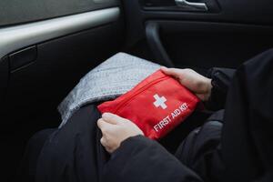 A person who is seated comfortably in a car holds a bright red first aid kit, demonstrating both preparedness and awareness of safety, which is a common and responsible practice in vehicles photo