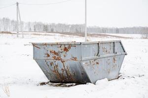 Amidst the vast, white expanse of a snowy field lies an old, rusty dumpster, its ruggedness standing out starkly against the tranquil and serene winter landscape that surrounds it photo