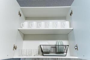 A wellstocked kitchen cabinet that is filled with a wide variety of cups and glasses, along with a practical dish drying rack that allows for easy access and optimal organization photo