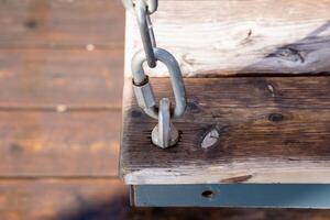 This image features a closeup view of a wooden swing, highlighting its beautiful surface, along with an attached chain that ensures it is securely suspended for enjoyment and safety photo