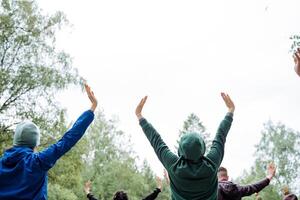 A group of happy people are gathered in a circle, raising their arms while surrounded by nature. Joyful gestures under the open sky, enjoying leisure time together on the grass photo