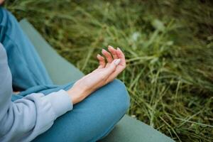 An individual practices meditation outside surrounded by nature, focusing on inner peace and balance, as depicted by their hands in a Zen gesture on a green mat photo