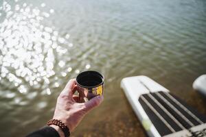 A mug from Terpmos in the hand of a person on the background of water, hiking on the water, a glass of tea in nature, a hand holding a mug with coffee. photo