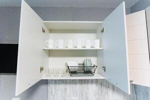 Inside a kitchen cabinet, open doors reveal a wellorganized shelf with various cups and glasses, showcasing a neatly arranged space that reflects care and attention to detail photo