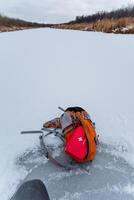 A backpack is casually sprawled on the smooth icy surface, right next to a gently flowing river, creating an intriguing scene amidst the beautiful snowy winter landscape surrounding it photo