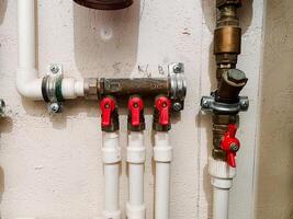 This image presents a detailed close up of a plumbing system featuring a network of white pipes accompanied by bright red valves, showcasing the intricacies of modern plumbing design photo