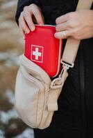 A person is standing while holding a bright red first aid kit firmly in their hand, ready to assist or provide urgent medical supplies if needed in case of an emergency situation photo
