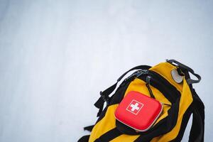 An essential first aid kit placed inside a yellow backpack, ideal for use in a snowy outdoor environment, perfect for any adventurer on their expedition or mountaineering journey photo