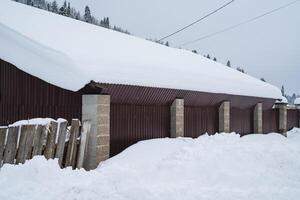 A picturesque snowy roof of a charming building can be seen, with a rustic wooden fence gracefully sitting in the foreground, creating a beautiful winter scene all around it photo