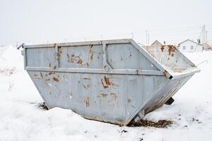 Amidst the biting chill of winter, a rusty old dumpster rests solitary in the thick white blanket of snow, highlighting its longneglected and forgotten condition in this frosty landscape photo