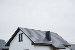 The house is white in color and features a stylish black roof along with a chimney that adds character to its overall design, making it attractive amidst a beautiful sky photo