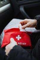 A person is in the process of opening a red first aid kit that is located inside a vehicle, specifically within a cars interior space, likely for an emergency situation photo