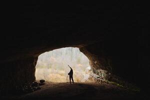 In a dimly lit cave, a solitary man stands still, completely lost in his thoughts as he gazes through the caves opening at the vast and breathtaking beauty of the outside world photo