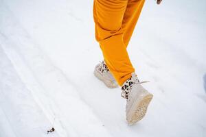 A person who is wearing bright yellow pants and stylish white boots is walking through the thick snow, enjoying the chilly winter day and the beauty of the icy landscape all around them photo