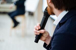 A speaker holds a black microphone in his hand, a person makes a speech on stage, a lecture with a microphone, an object that transmits a voice. photo