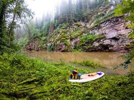 A surfboard is currently resting on the sandy shoreline of a river located in the tranquil woods, creating a picturesque scene that blends adventure with natures beauty photo