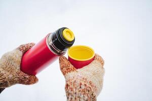 A person is diligently and carefully pouring a steaming, hot cup of coffee from a thermos, more commonly known as a vacuum flask, into a waiting mug, ensuring that not a drop spills photo