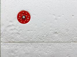 CloseUp of a Red Circular Object on a Textured White Surface with Subtle Patterns photo