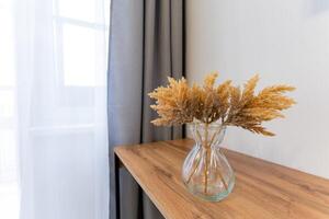A vase filled with dried flowers is sitting on a wooden table photo
