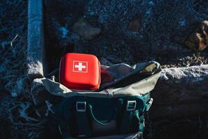 The red box of the first aid kit with medicines is in the backpack of the tourist, essential equipment, a mini first aid kit, a hard box. photo