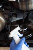 A person is seen wearing blue gloves as they are diligently cleaning a stove using a spray bottle filled with cleaning solution to ensure its sparkling and free of grime photo