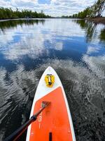 Orange and white paddle board drifts on calm lake waters, blending with serene nature, exuding tranquility and connection with the surroundings. Calming and harmonious scene photo